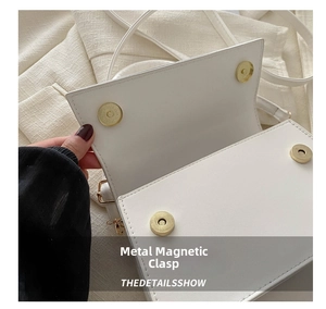 Close-up of golden metal magnetic buckle and fine stitching on white leather handbag