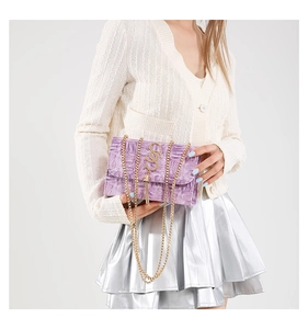 Détail du sac à chaîne violet gaufré avec pompon doré porté par un mannequin en studio