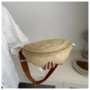 Gros plan du sac banane en paille tressée avec zip argenté et bandoulière marron réglable