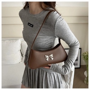 Close-up of a coffee brown leather baguette bag featuring a silver metal bow detail