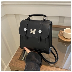 Detail of silver butterfly hardware and rivet straps on a black structured leather handbag