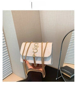 Détail d'un sac à bandoulière blanc en similicuir avec logo à pompon doré et chaîne