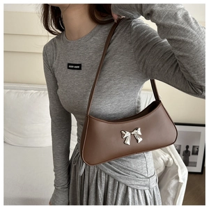 Detailed close-up of a brown leather baguette bag featuring a silver bow accent
