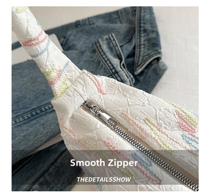 Detail of embroidered canvas bag showing wavy patterns and smooth silver zipper closure