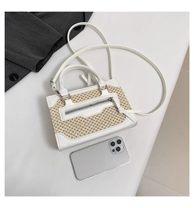Vue de dessus d'un sac bandoulière blanc crème tissé à côté d'un téléphone portable