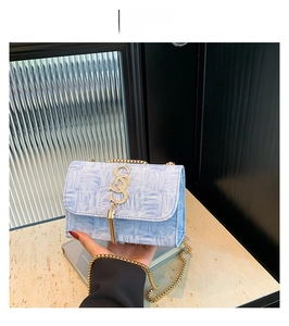 Détail du sac bandoulière bleu texturé avec logo S doré et accessoire de chaîne