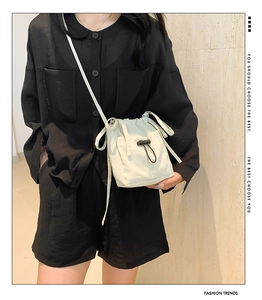 Detail of cream drawstring nylon crossbody bucket bag with functional front buckle pocket