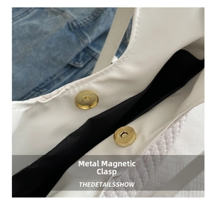 Detail shot of the golden magnetic hardware clasp on a white woven tote bag