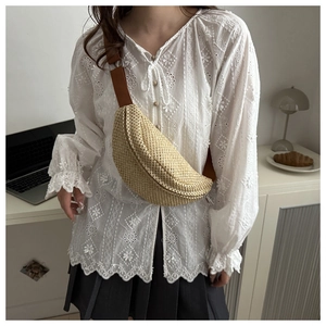 Détail d'un sac banane en paille tressée beige avec sangle marron porté par un mannequin