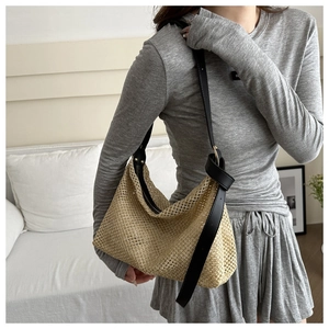 Détail d'un sac cabas en paille tissée avec bandoulière en cuir noir et boucles