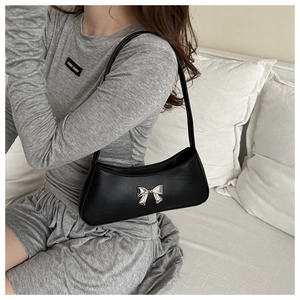 Detalle de un bolso de hombro en cuero PU negro con un lazo decorativo de metal plateado