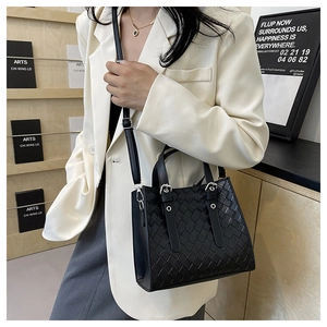 Detail of a black woven tote bag with adjustable shoulder strap on a white blazer model