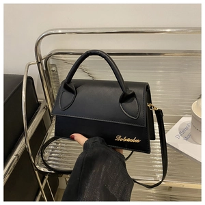 Detail of black leather handbag with gold metal logo and adjustable shoulder strap