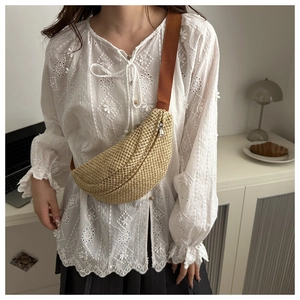 Close-up of woven straw crescent chest bag with adjustable brown strap on a white lace top