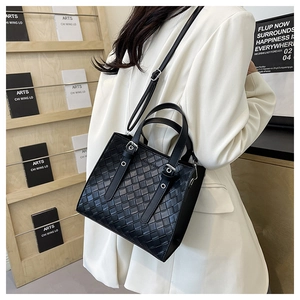 Detail of black woven texture handbag worn with white blazer against a minimalist background