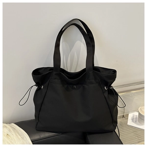 Detail of black tote bag featuring side drawstrings and snap button on a leather bench
