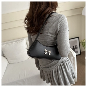 Detail of black leather underarm bag featuring a silver bow metal ornament on the side