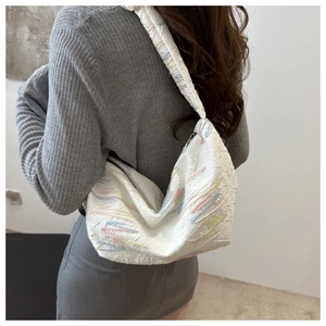 Detail of white pleated hobo bag with colorful pastel embroidery on model shoulder