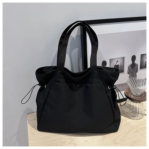 Detail of minimalist black tote bag featuring metal snap button and side drawstring closure