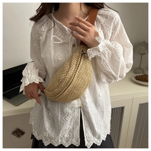 Détail d'un sac à bandoulière tissé en paille beige avec sangle marron porté par un modèle