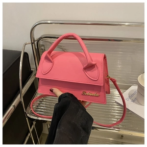 Detail shot of bright pink leather crossbody bag featuring gold metal logo and handle