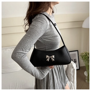 Detail of black matte leather underarm bag with a silver metallic bow and single strap