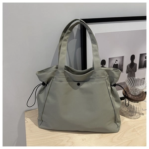 Close-up of a sage green tote bag with drawstring details on a wooden surface