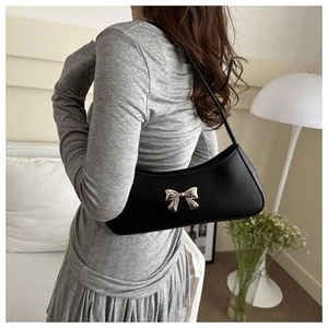 Side view of a black underarm bag with a silver butterfly ornament on a model