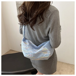 Détail du sac hobo plissé bleu clair avec coutures colorées sur l'épaule du mannequin