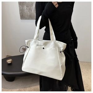 Detail of white large capacity tote bag featuring side drawstrings and a black button