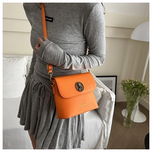 Détail d'un sac seau orange vif avec boucle en métal rétro et logo de marque sur le devant