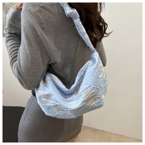 Gros plan d'un sac croissant bleu clair avec broderies colorées et détail de bandoulière nouée