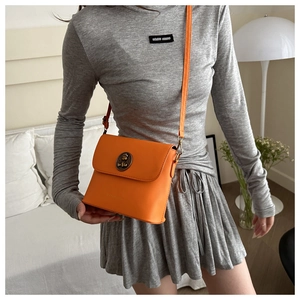 Vue détaillée du sac bandoulière orange vif avec logo métallique en bronze gaufré