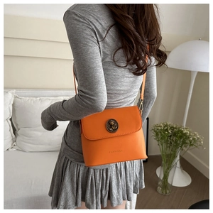 Detail of orange leather crossbody bag with vintage cat motif metal buckle and strap