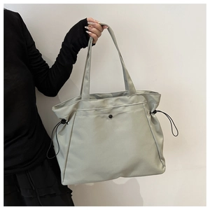 Close-up of the light green tote bag with adjustable side drawstrings and metal snap pocket