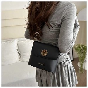 Detail view of the black leather bucket bag with golden metal emblem and branding