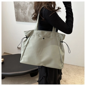 Detailed view of grey-green nylon tote bag with adjustable side drawstrings and metal snap