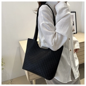 Detail of a black woven tote bag with 3D texture and minimalist leather straps
