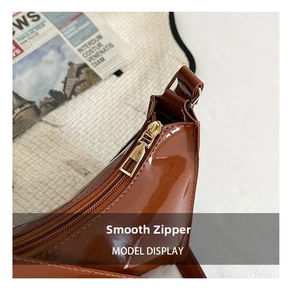 Detail of smooth gold zipper and brown glossy patent leather on chic shoulder bag
