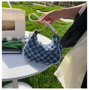 Détail du sac baguette en jean à damier bleu avec bords effilochés et anse blanche