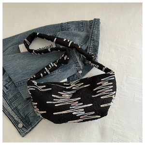 Détail du sac dumpling en nylon noir avec broderies ondulées et bandoulière rembourrée