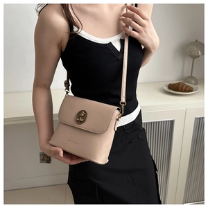 Détail du sac seau beige avec emblème de lion doré et fine bandoulière en cuir