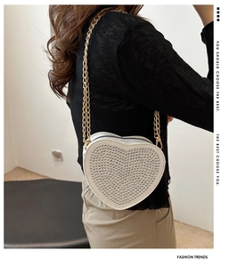 Detail of heart-shaped crossbody bag with metal rivets and golden double chain straps