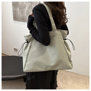 Minimalist light green tote bag with adjustable side drawstrings shown on a model