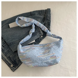 Détail du tissu en nylon plissé bleu clair avec broderies colorées sur un sac hobo