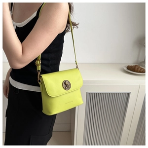 Détail du sac bandoulière vert néon avec emblème en laiton et bandoulière réglable