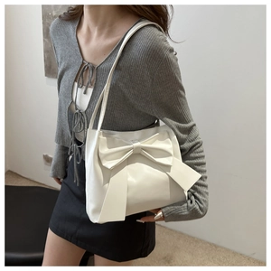 Detail of off-white tote bag featuring a large bow and long shoulder straps for underarm wear