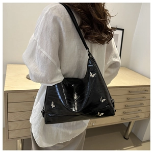 Side view of black glossy shoulder bag with silver butterfly charms on a white shirt