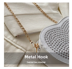 Detail of white heart crossbody bag featuring silver studs and gold chain lobster clasp