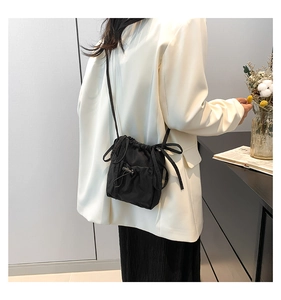 Detail of black drawstring nylon crossbody bag showing ribbon accents and adjustable strap